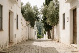 A quiet cobblestone village street in Benahavis with whitewashed and stone walls, mature olive and cypress trees, representing inland privacy in the Costa del Sol Golden Triangle