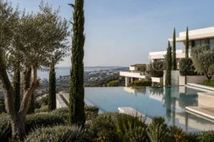 Architectural detail of a Costa del Sol residential resort with infinity pool, mature cypress and olive landscaping and the Mediterranean in the distance, representing service-led family living on the coast
