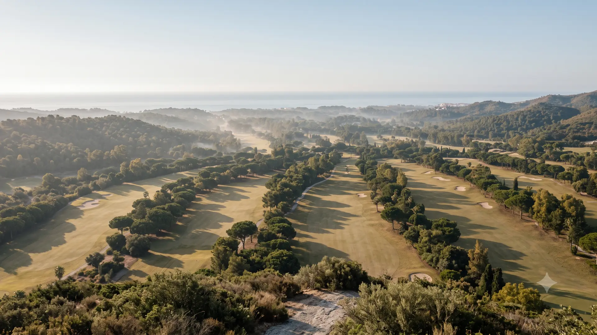Elevated morning view over the golf corridor between Elviria and Las Chapas in Marbella East, with mist in the valley and the Mediterranean beyond