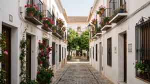 Cobbled street in Marbella Old Town with whitewashed walls, geranium-filled balconies and an orange-tree square with a fountain at the far end