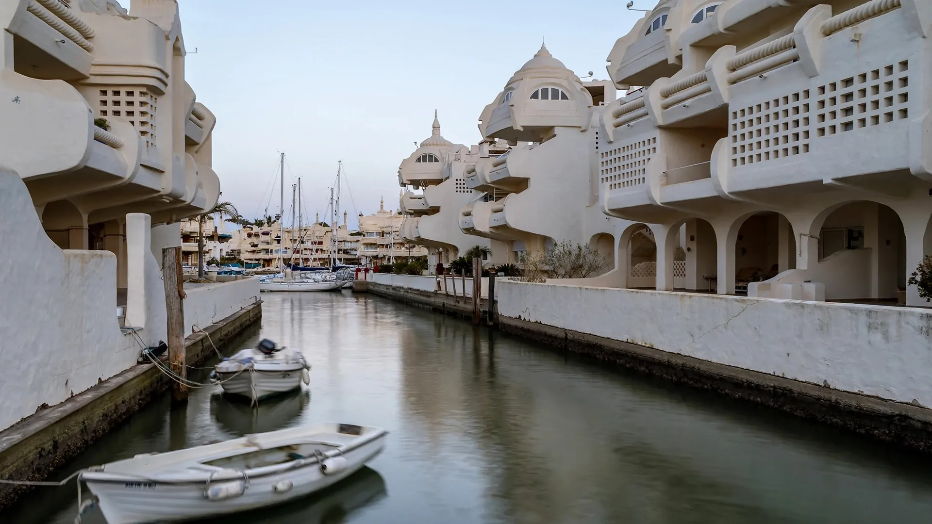 A water channel at Puerto Marina in Benalmadena, lined with the marina's distinctive white sculptural apartment architecture and small moored boats