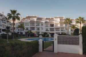 Andalusian residential apartment complex with communal pool, palm trees and entrance gate with mailboxes